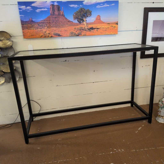 Black metal console table against a white wall with a scenic painting of a desert landscape.
