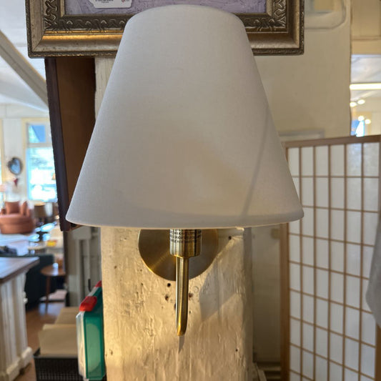 Wall-mounted lamp with white shade and gold base in a room setting