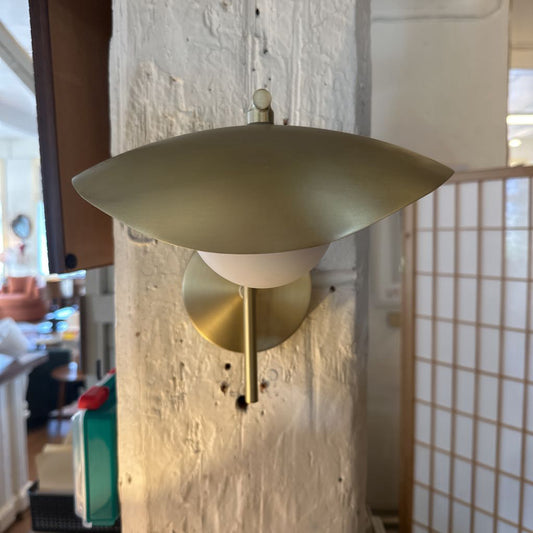 Gold wall sconce on a textured wall with a blurred indoor background