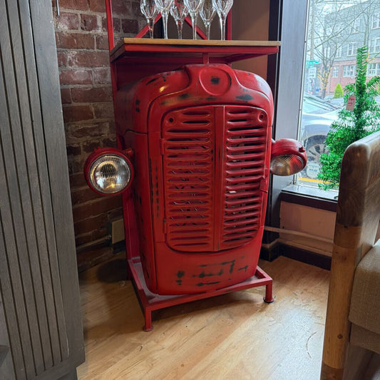 Red vintage tractor-shaped object with glass holders indoors.