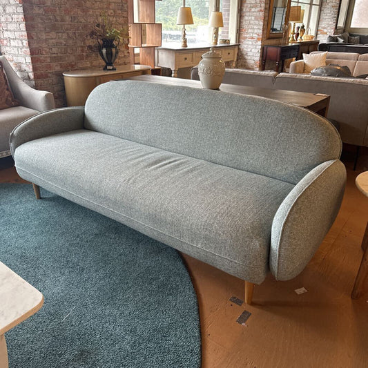 Gray sofa in a living room setting with a brick wall and wooden floor.