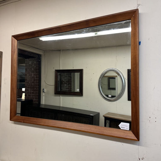 Large wooden-framed mirror on a wall with smaller mirrors in the background.