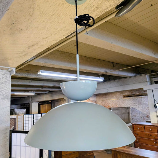 Light blue pendant lamp hanging from a ceiling in an industrial-style room with wooden beams and exposed pipes.