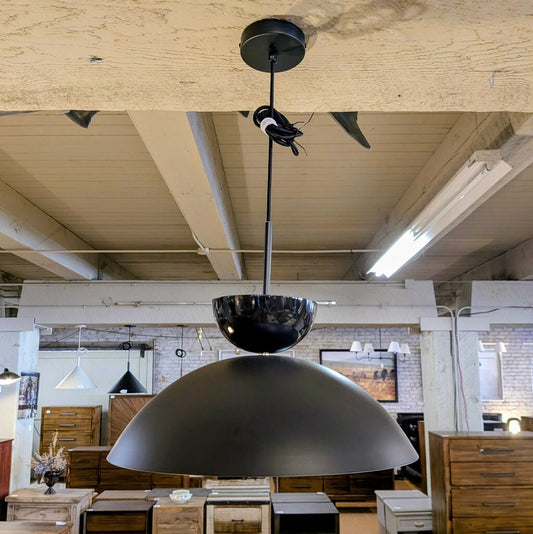 Large black pendant light hanging from a wooden ceiling in an indoor setting.