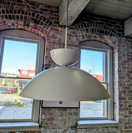 White pendant light hanging from a brick wall with windows in the background
