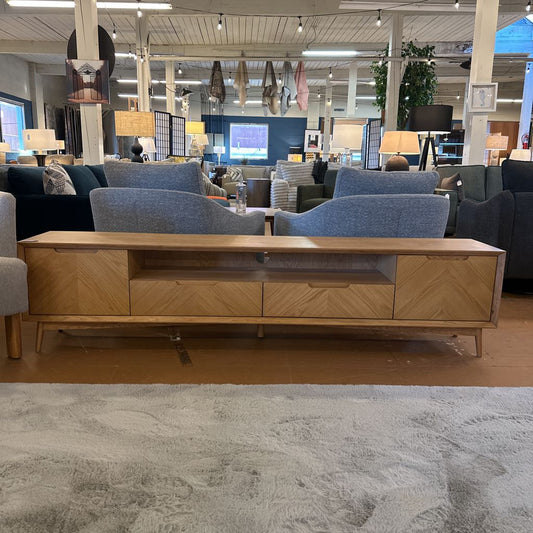 Wooden TV stand in a furniture store with blue sofas and various decor items.