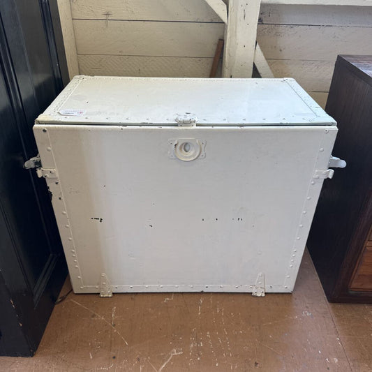 White metal storage box on a wooden floor with a wooden wall in the background