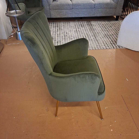 Green armchair with gold legs on a brown floor.