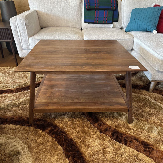 Wooden coffee table in front of a beige sofa with colorful cushions on a patterned rug.