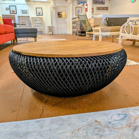 Round coffee table with wooden top and black woven base in a showroom setting