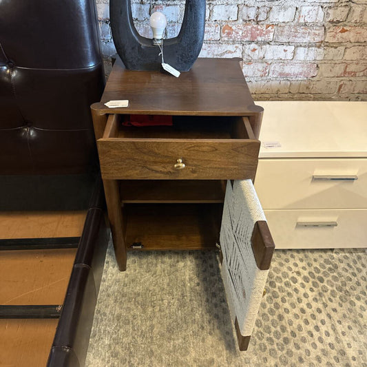 Wooden nightstand with a drawer in a room with furniture and a brick wall.