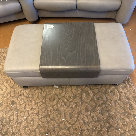 Gray ottoman with a wooden top on a patterned carpet