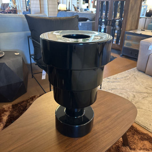 Black cylindrical object on a wooden table with a blurred indoor setting