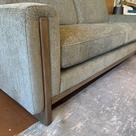 Gray textured sofa with wooden armrests on a gray rug.