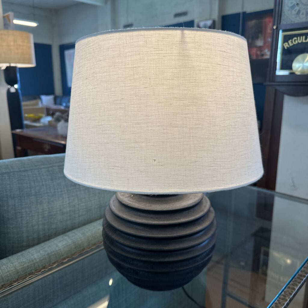 Lamp with a textured white shade on a reflective surface in an indoor setting