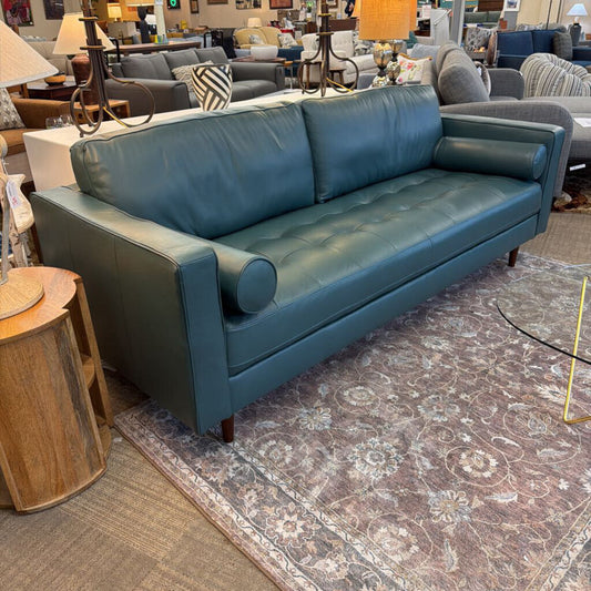 Blue leather sofa in a furniture store with various other furniture pieces in the background.