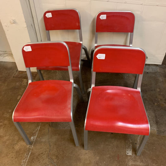 Four red chairs with metal frames on a concrete floor.