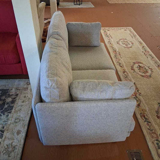 Gray sofa with a pillow on a wooden floor with patterned rugs.