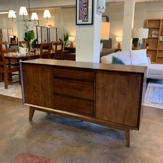 Wooden sideboard in a furniture store with a dining area and living room in the background.