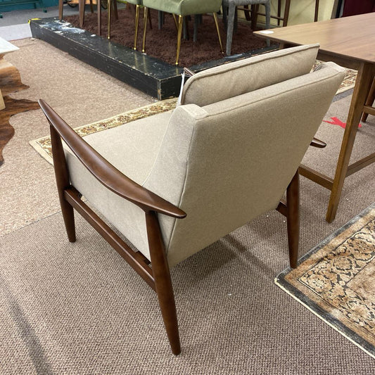 Beige armchair with wooden arms and legs in a room with furniture and decor.