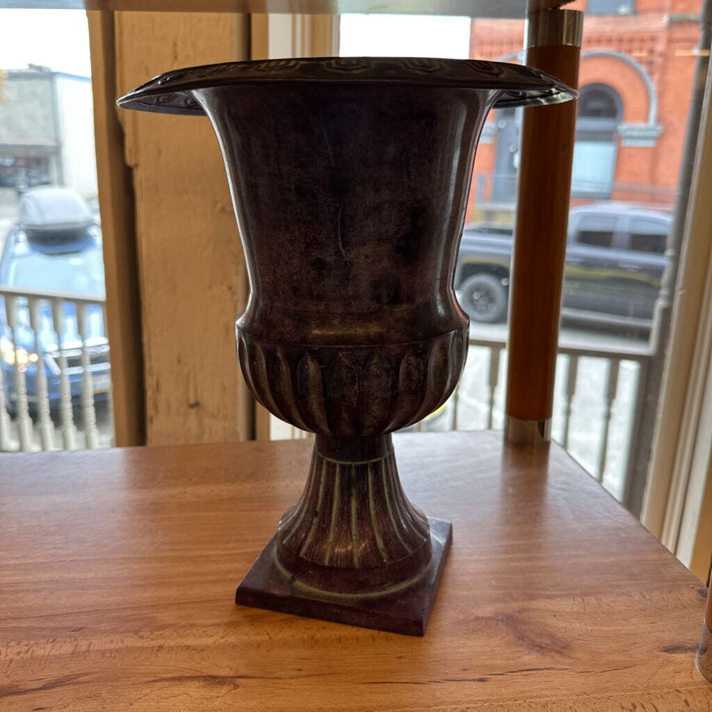 Decorative urn on a wooden surface with a window view in the background
