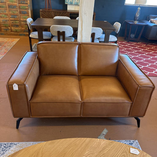 Brown leather sofa in a room with a dining table and chairs.