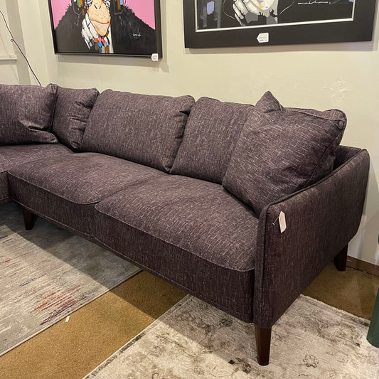 A dark grey, L-shaped fabric sectional sofa with tapered wooden legs, styled on a patterned rug beneath two pop-art paintings of chimpanzees wearing headphones.