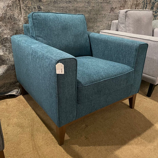 Contemporary armchair upholstered in a blue marled fabric, featuring a thick seat cushion, square arms, and a wooden base with tapered legs.