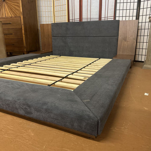Gray upholstered bed frame with wooden slats on a wooden floor.