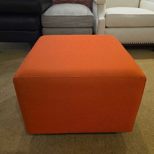 Orange cube-shaped ottoman in a room with other furniture.