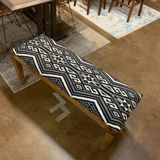 Wooden bench with a black and white patterned cushion in a room with a rug and chair.