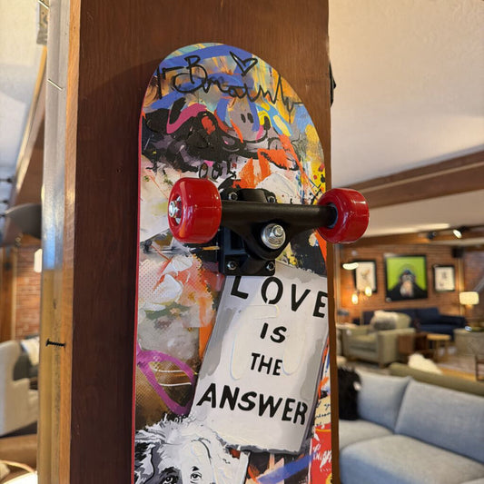 A decorative skateboard deck mounted vertically on a wooden pillar, featuring a colorful street-art style collage with Albert Einstein holding a sign that reads 'Love is the Answer'