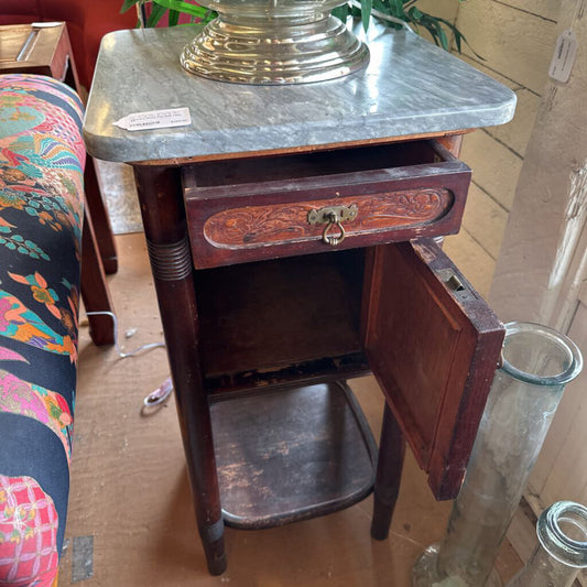 Wooden side table with marble top and open drawer in a room setting