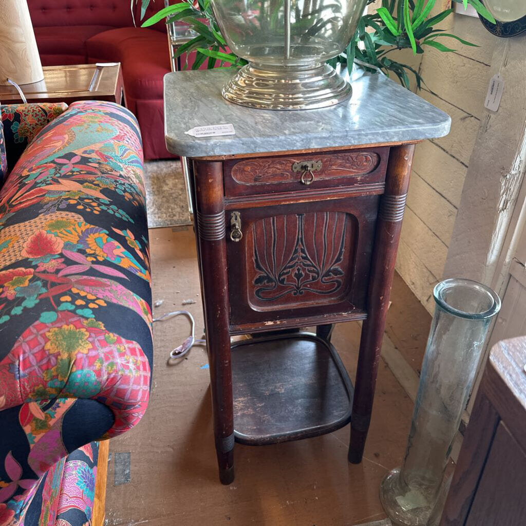 Vintage wooden side table with marble top next to a colorful floral-patterned sofa.