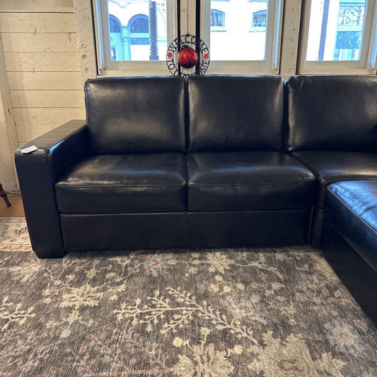 Black leather sectional sofa in a room with a patterned rug and window.