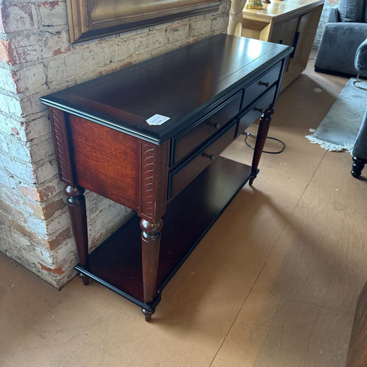 Wooden console table with dark finish against a brick wall.