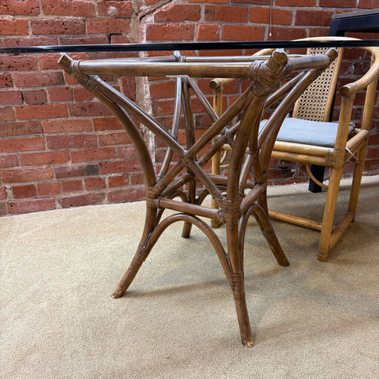 Rattan dining table with glass top against a brick wall.
