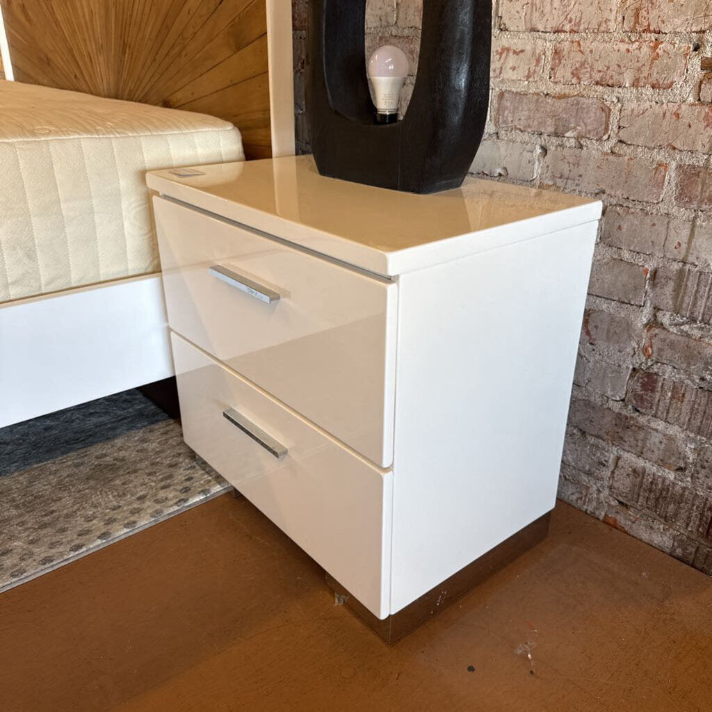 White dresser with two drawers against a brick wall.