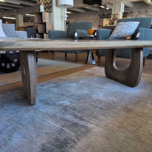 Large wooden dining table in a showroom setting with chairs and decor.