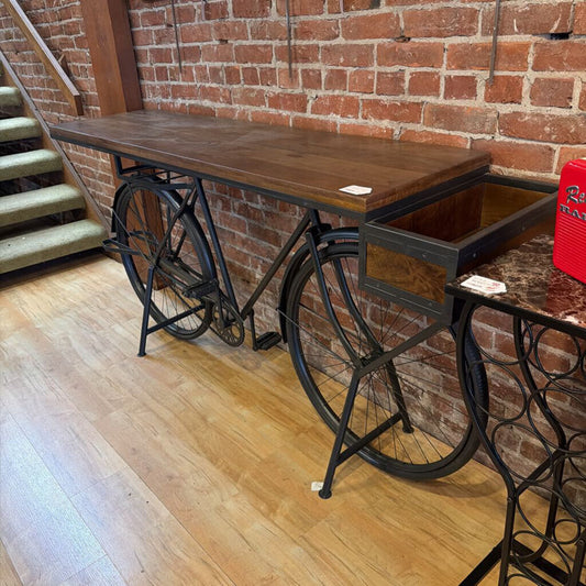 Wooden table with bicycle legs against a brick wall