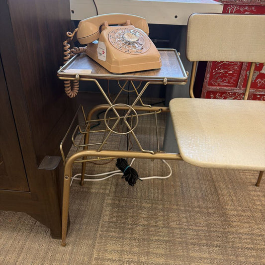 Vintage beige rotary phone on a small table with a chair in a room setting.