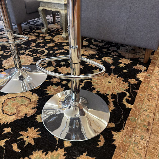 Chrome bar stools on a patterned rug with a gray sofa in the background