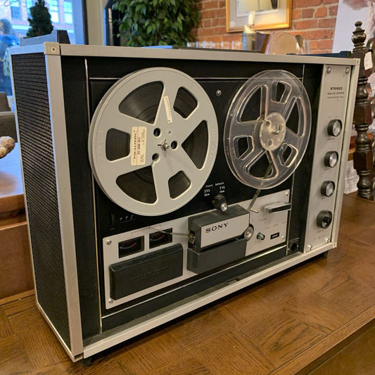 Vintage reel-to-reel tape recorder on a wooden surface with a blurred indoor background