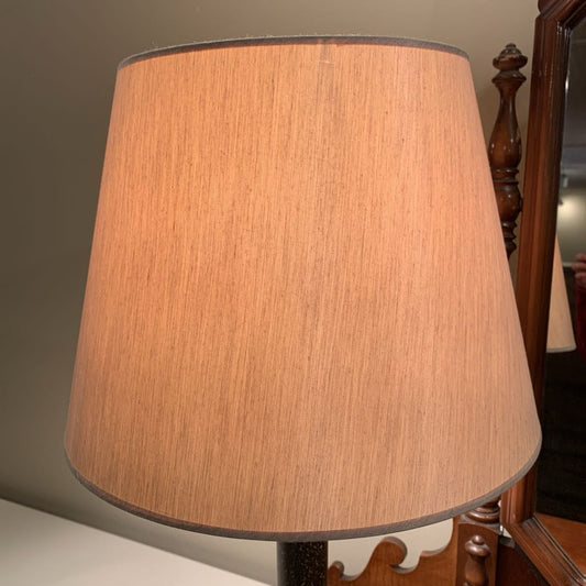 Brown lampshade on a wooden stand against a neutral wall.