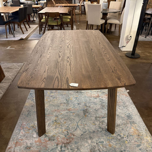 Wooden dining table in a showroom setting with chairs and flooring visible
