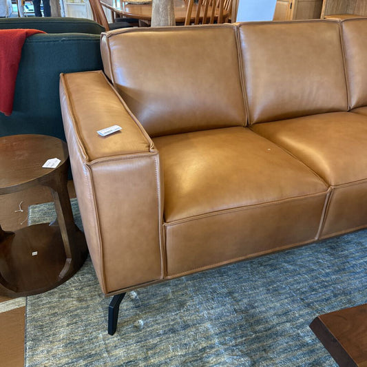 Brown leather sofa in a room with a blue carpet and wooden furniture.