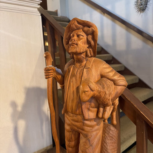Wooden sculpture of a man with a beard holding a sheep on a staircase