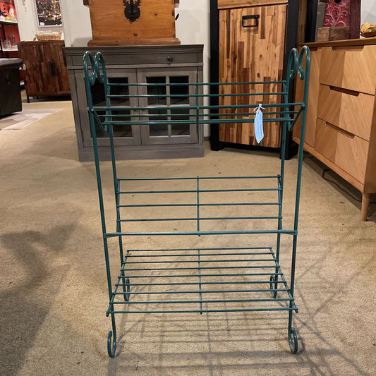Green metal baker's rack in a store setting with wooden furniture.