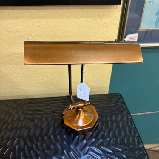 Gold desk lamp on a textured black surface with a yellow wall in the background