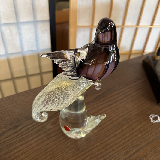 Glass sculpture of a bird on a stand with a blurred background